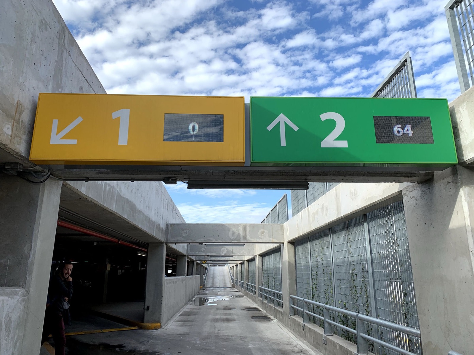 Overhead yellow and green signs in a car park showing 0 free spaces on level 1 and 64 on level 2.